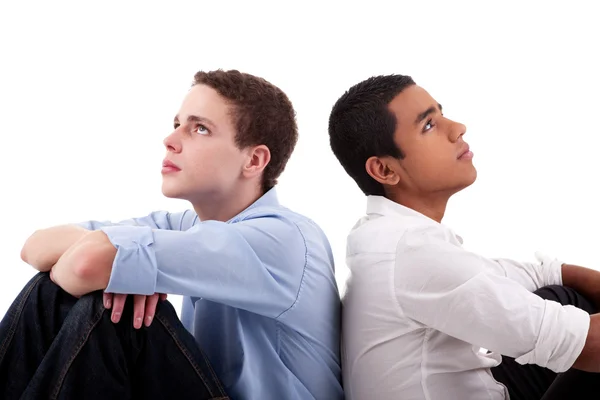 Двоє молодих чоловіків різних кольорів, сидячи на підлозі, спині до спини, ізольовані на білому, студійний знімок — стокове фото