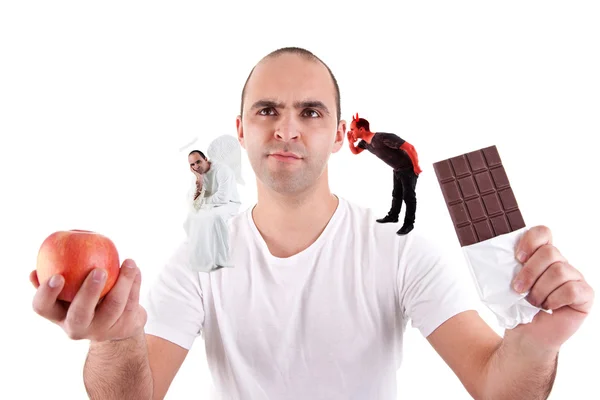 stock image Young man torn between eating an apple and a chocolate,between the devil and angel, on white
