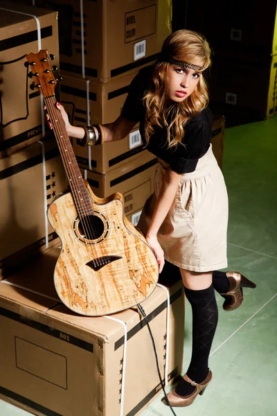 Mooie jonge vrouw met een klassieke gitaar in een magazijn met vakken zoals scenario — Stockfoto