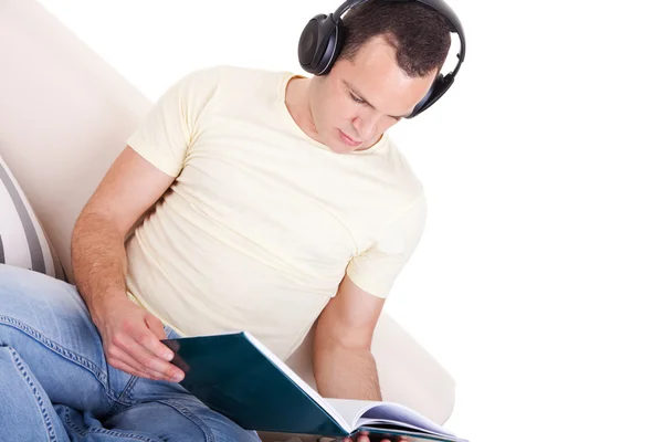 stock image Man reading and listening music with headphones on couch, isolated on white background, studio shot