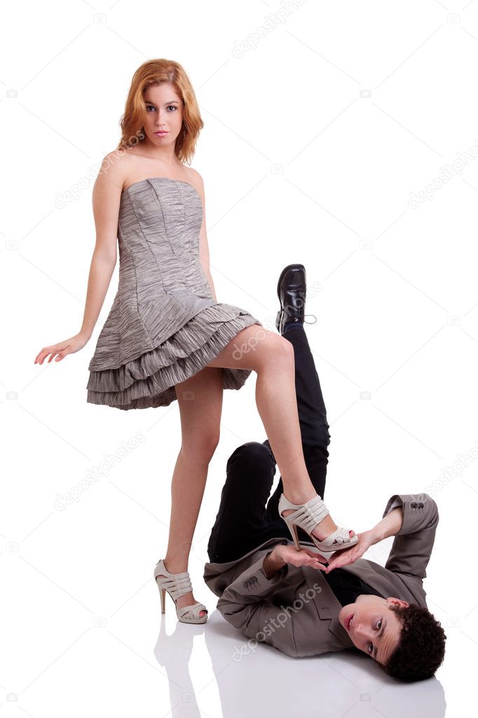 Beautiful young woman stepping on a young man, isolated on white, studio shot