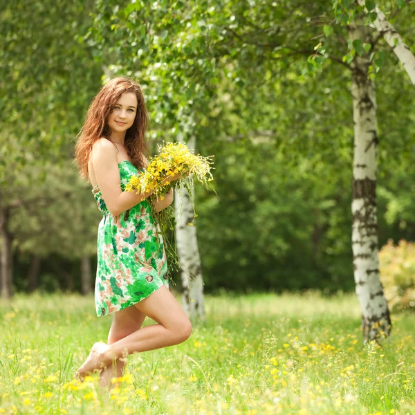 Joven pelirroja en el parque con flores — Foto de Stock