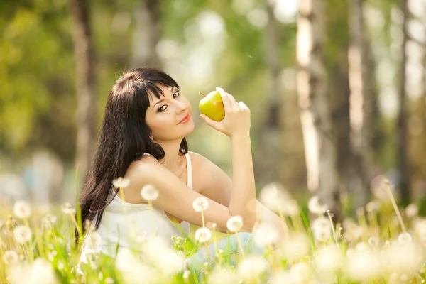 Femme mignonne manger la pomme dans le parc avec des pissenlits — Photo