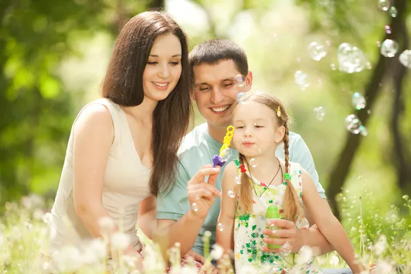 Felice madre, padre e figlia che soffiano bolle nel parco — Foto Stock