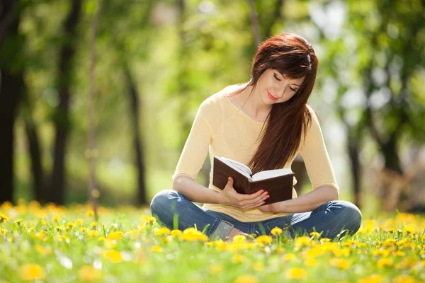 Ung kvinna läser en bok i parken med blommor Stockbild