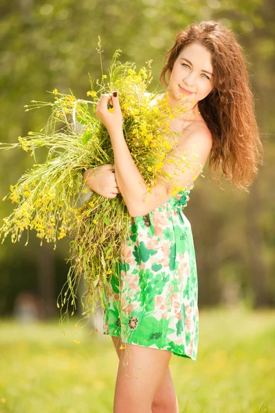 Giovane rossa donna nel parco con fiori — Foto Stock