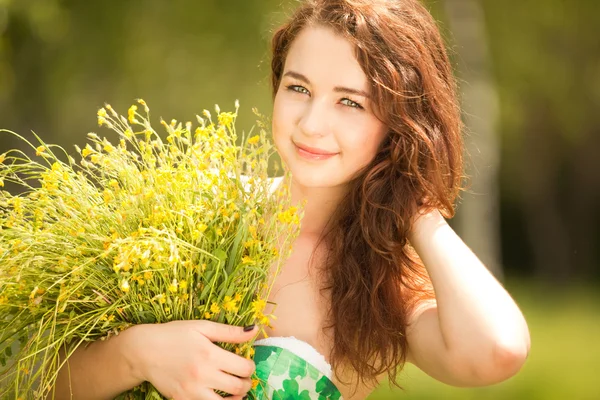 Giovane rossa donna nel parco con fiori — Foto Stock