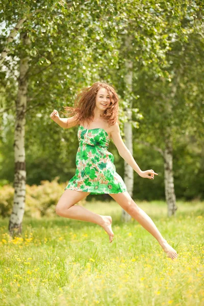 Küçük kızıl saçlı kadın çiçeklerle parkta atlama — Stok fotoğraf