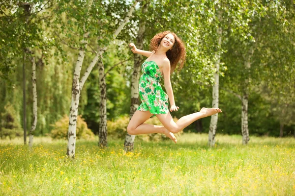 Young redhead woman jumping in the park with flowers — Stock Photo, Image