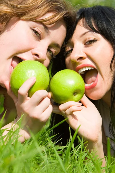 Ładne kobiety jedzenie zielone jabłka na polanie lato — Zdjęcie stockowe