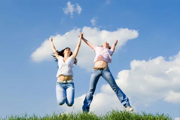Dos mujeres felices saltando sobre la hierba verde — Foto de Stock