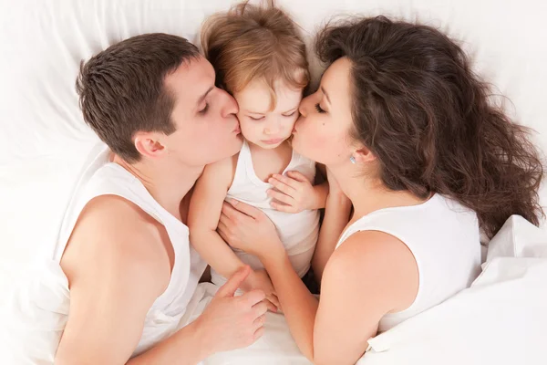 Lycklig familj, mor, far och dotter på vita sängen — Stockfoto