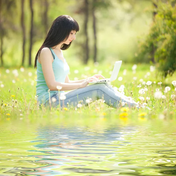 Ładny kobieta z białym laptopa w parku z mniszek lekarski — Zdjęcie stockowe