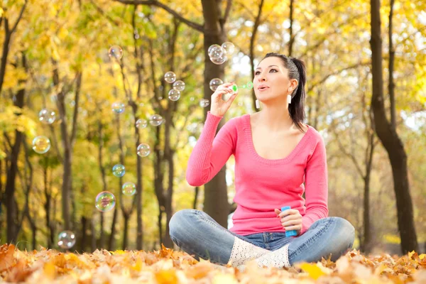 Young woman blowing soap bubble in the autumn park — Stock Photo, Image