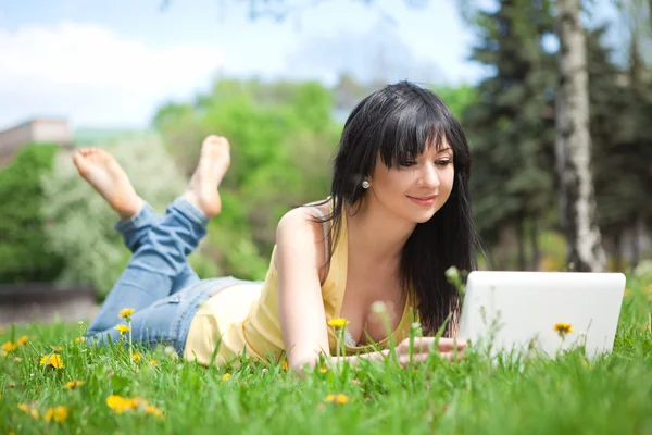 Cute woman with white laptop in the park with dandelions — Stock Photo, Image