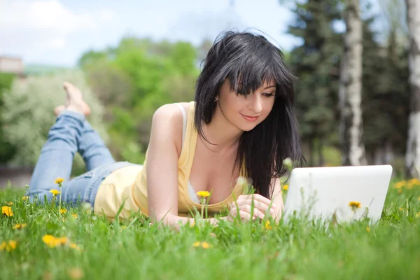 Leuke vrouw met witte laptop in het park met paardebloemen — Stockfoto