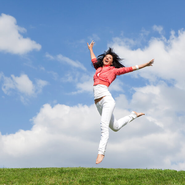 Pretty young woman jumping on green grass