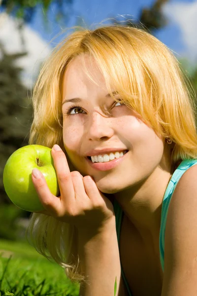 Красивая женщина ест зеленое яблоко на летней поляне — стоковое фото