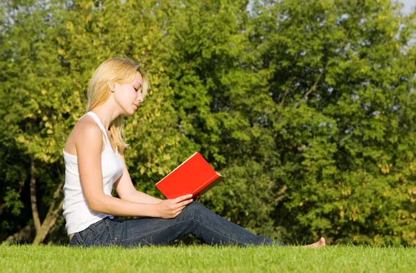 Jonge blonde leest boek in het park — Stockfoto