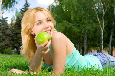 Pretty woman eating green apple on the summer glade clipart