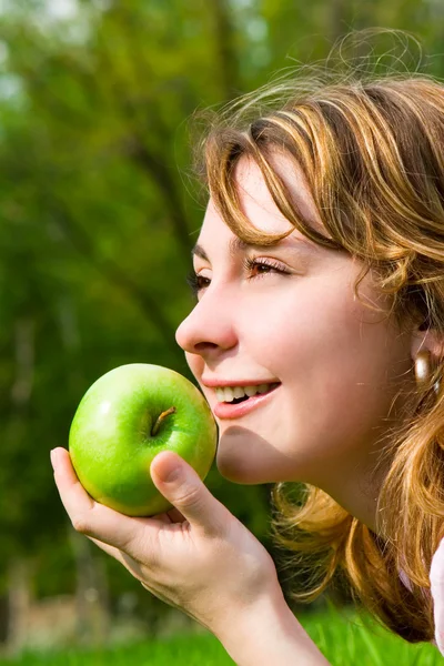 Ładna kobieta jedzenie zielone jabłko na polanie lato — Zdjęcie stockowe