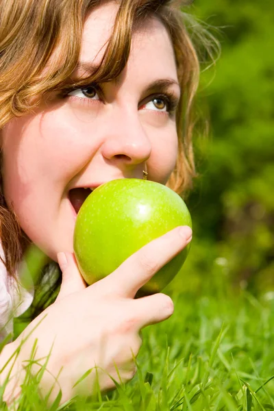 夏の空き地に緑のリンゴを食べてきれいな女性 — ストック写真