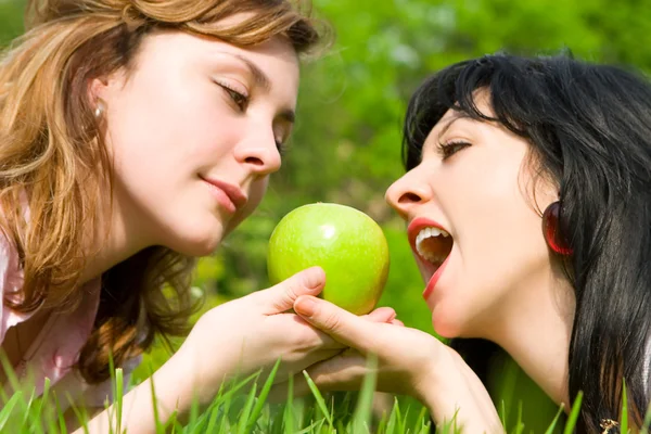 Ładne kobiety jedzenie zielone jabłka na polanie lato — Zdjęcie stockowe