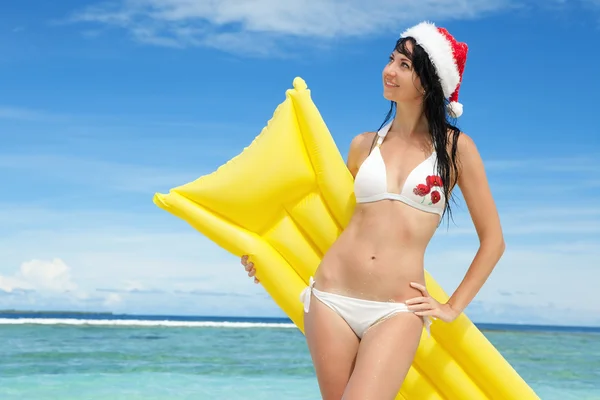 Happy santa žena s nafukovací matrace na pláži. Vánoce — Stock fotografie