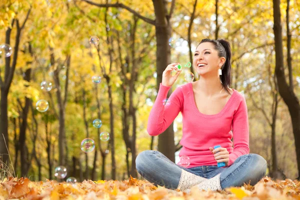 Young woman blowing soap bubble in the autumn park — Stock Photo, Image