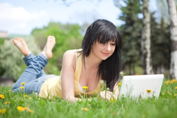 Carino donna con computer portatile bianco nel parco con denti di leone — Foto Stock