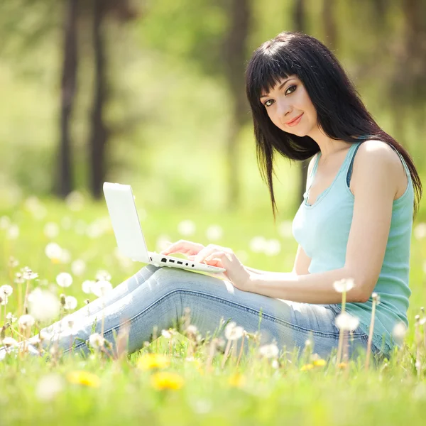 Leuke vrouw met witte laptop in het park met paardebloemen — Stockfoto