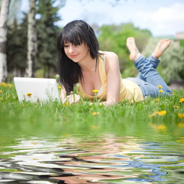 Милая женщина с белым ноутбуком в парке с одуванчиками — стоковое фото