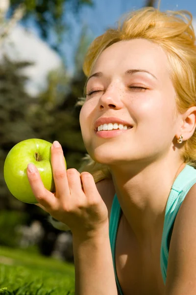Красивая женщина ест зеленое яблоко на летней поляне — стоковое фото