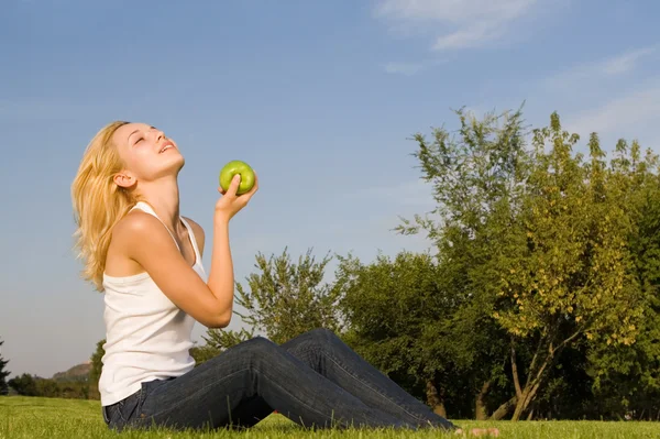 在夏天的林间空地上吃青苹果的漂亮女人 — 图库照片