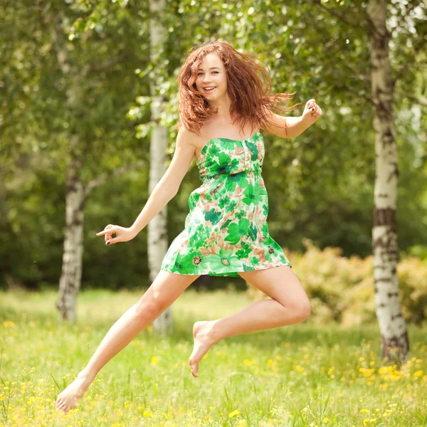 Jonge redhead vrouw springen in het park met bloemen — Stockfoto