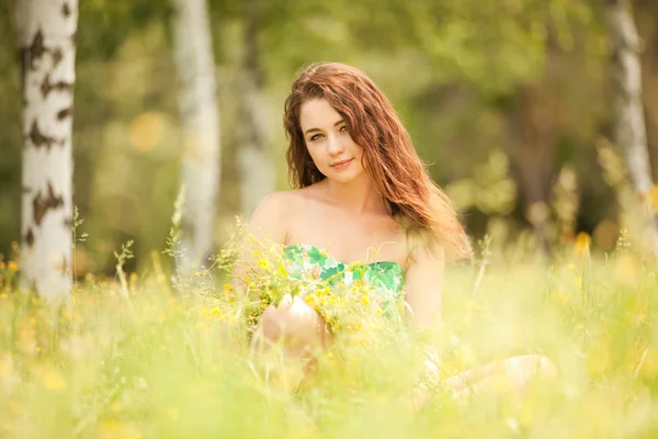 Unga rödhårig kvinna i parken med blommor — Stockfoto