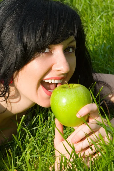 夏の空き地に緑のリンゴを食べてきれいな女性 — ストック写真