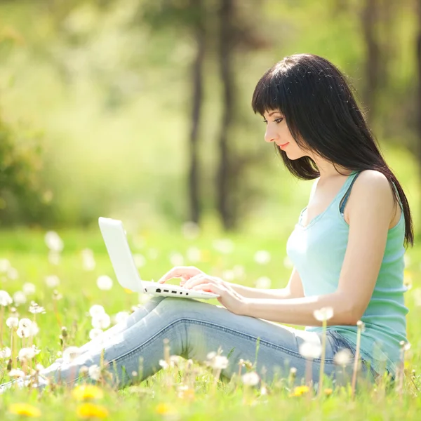 Χαριτωμένο γυναίκα με λευκό laptop στο πάρκο με πικραλίδες — Φωτογραφία Αρχείου