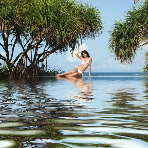 Giovane donna seduta accanto alla piscina sulla spiaggia — Foto Stock