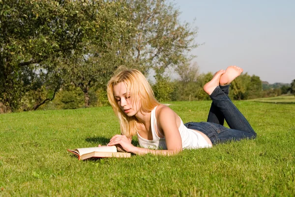 若いブロンドは公園で本を読みます — ストック写真