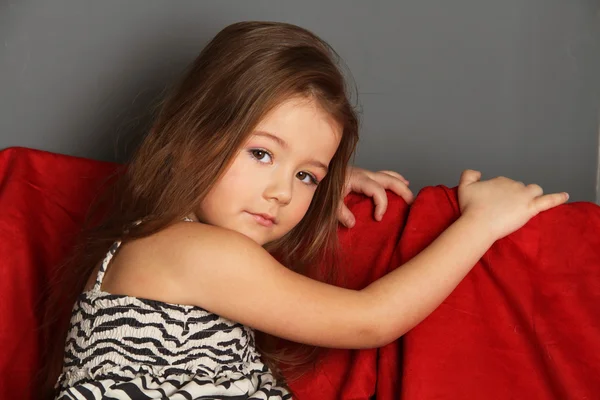 Little girl on a red sofa — Stock Photo, Image