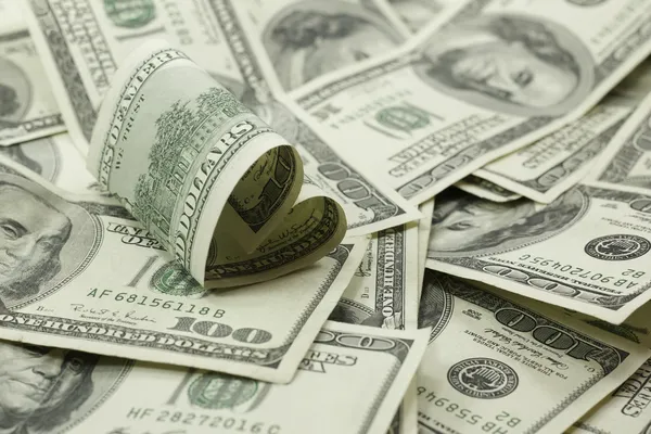 Heart shaped 100 dollar bill on pile of money — Stock Photo, Image