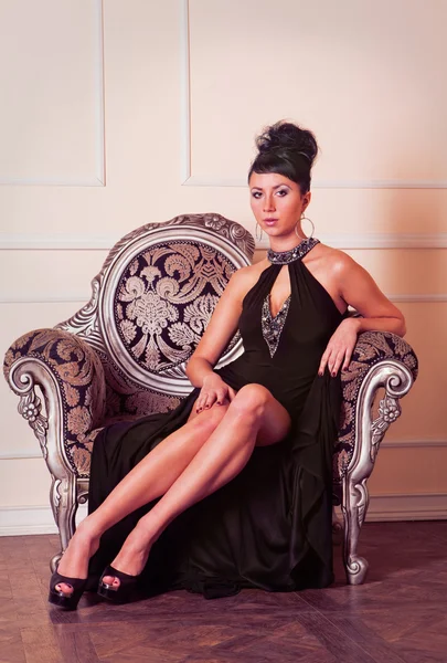 Молодая брюнетка в черном платье сидит на диване — стоковое фото