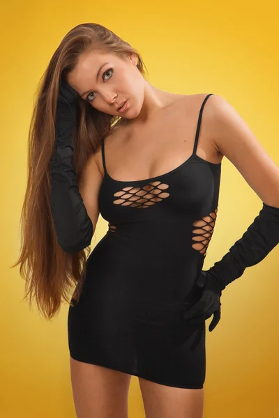 Cute young brunette girl in black sexy dress on yellow background — Stock Photo, Image