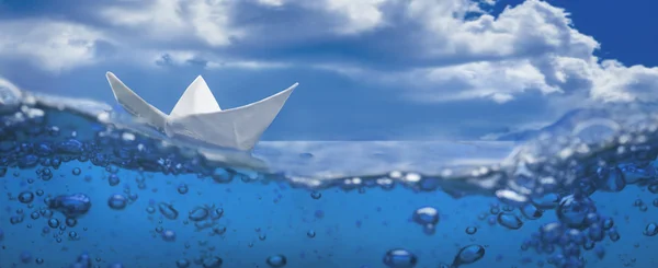 Papier bateau éclaboussure avec des bulles naviguant dans l'eau bleue et le ciel Images De Stock Libres De Droits