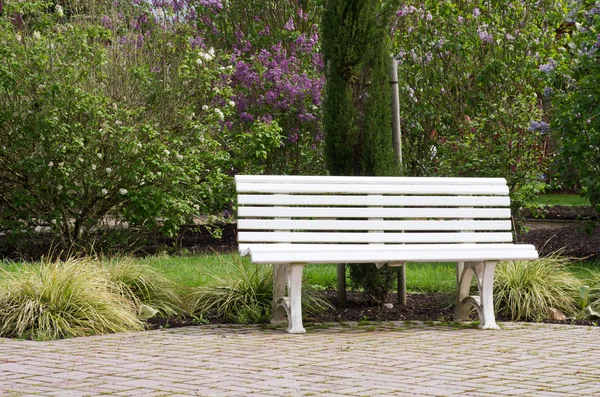 White garden bench on red paved walk — Stock Photo, Image