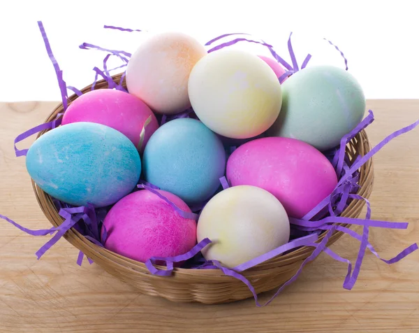 Wicker basket of colored eggs with purple straw — Stock Photo, Image