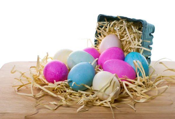 Cesta pequeña con huevos de colores derramados en paja —  Fotos de Stock