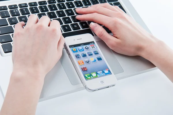 Biały iphone 4 w rękach kobiet obok macbook pro — Zdjęcie stockowe