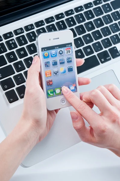 Белый iphone 4 в женских руках рядом с Macbook Pro — стоковое фото